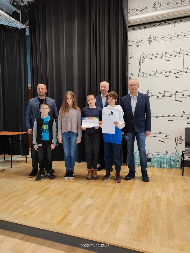 Stojące dzieci i dorośli trzymające dyplomy na zawodach w szachy pozujące do zdjęcia